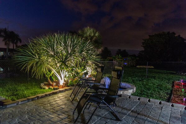An outdoor patio area with a table and chairs, surrounded by a garden with palm trees and a fence. - Perfect getaway - Canal front, close to the beach (Rotonda West)
