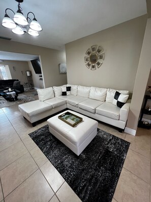 Relax in this stylish living room with a large L-shaped sofa, ottoman, and decorative chandelier.
