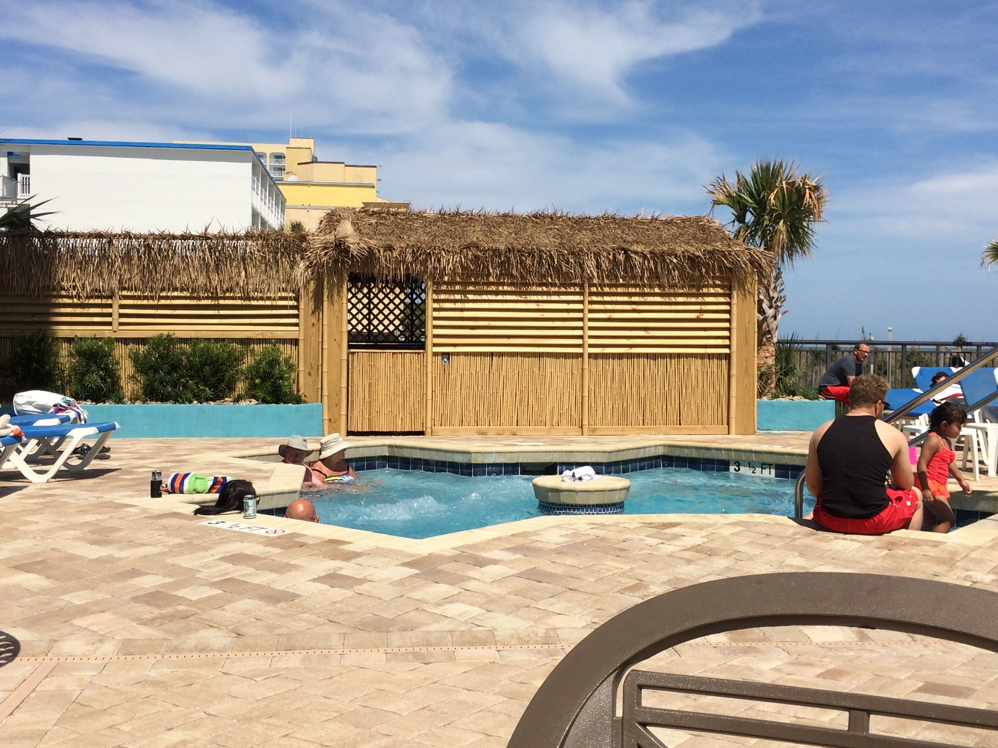 Un espace piscine comprenant des chaises longues, une petite piscine et une structure en bois surmontée d’un toit de chaume.