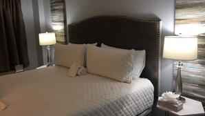 Una cama bien hecha con cabecera acolchada, dos lámparas de noche y una toalla doblada sobre la cama.