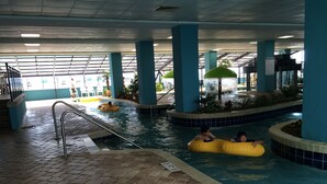 Una piscina interior con suelo de baldosas, pilares azules y una zona cubierta con techo.
