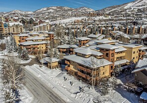 A snow-covered resort with multiple buildings, a ski slope in the background, and a clear sky.