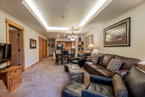 A spacious living room with a leather couch, wooden cabinets, a television, and a dining area with a chandelier.