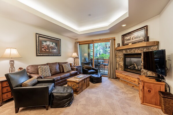 A cozy living room with a fireplace, leather furniture, and a large window overlooking a patio.