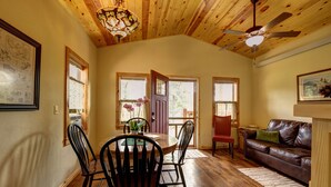 A dining area with a wooden table and chairs, a ceiling fan, and a view through a door to the outside.