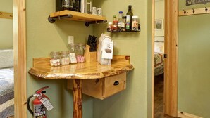 A kitchen with a wooden table, shelves with glassware, and a fire extinguisher.