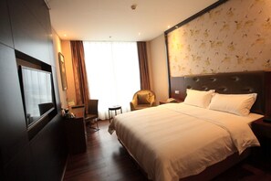A hotel room with a large bed, a desk with a chair, a small table, and a window with curtains.