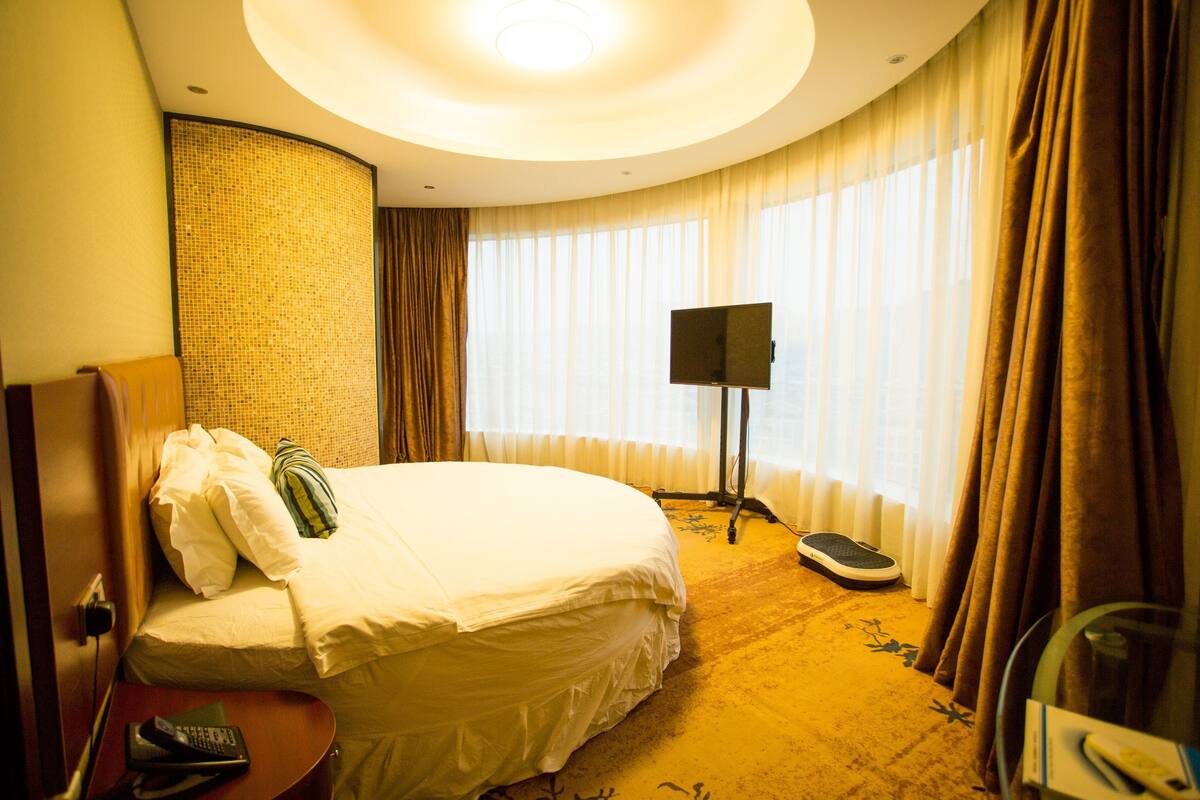 Habitación de hotel con cama, televisor sobre un mueble, balanza y control remoto sobre una mesa.