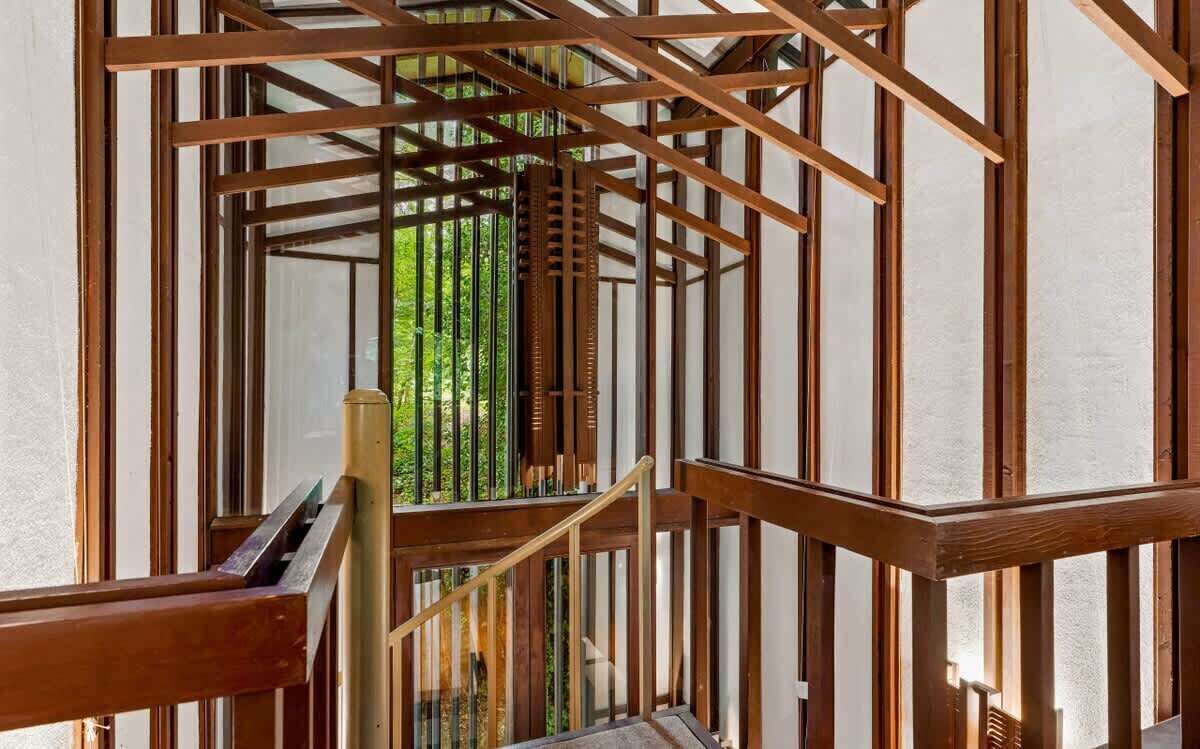 Una escalera de madera con barandilla de metal que lleva a un vidrio con vista a la vegetación.