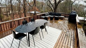 A wooden deck with a round table and chairs, a sofa, and a grill.