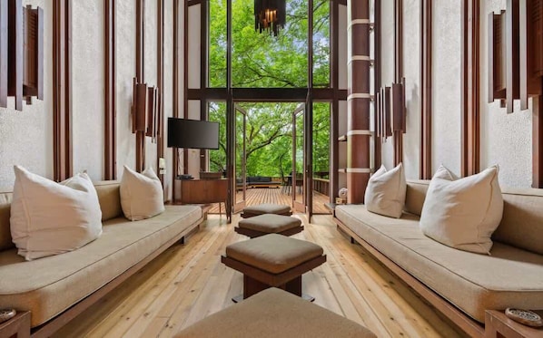 Ein modernes Interieur mit Holzboden, zwei Sofas mit Kissen, einem Flachbildfernseher und einem großen Fenster mit Blick auf Grünflächen.