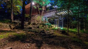 Une cabane en bois rustique, dotée de fondations en pierre, entourée d’une forêt.