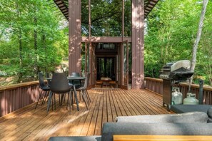 A wooden deck with a pergola, outdoor seating, and a barbecue grill.