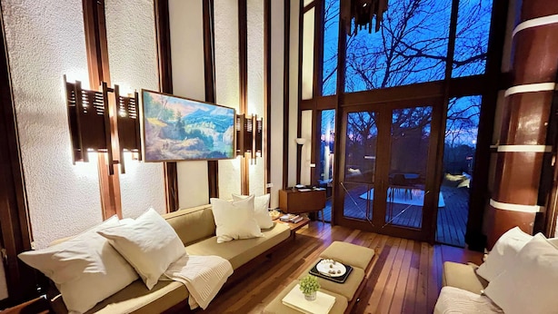 A modern living room with a large window, a painting, and a wooden floor.