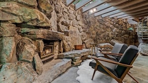 A stone fireplace with a fire, surrounded by a stone wall and a seating area with chairs.
