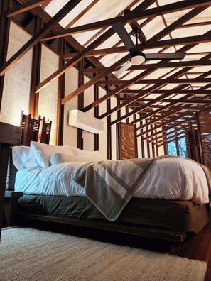 A bed with white bedding in a room with exposed wooden beams and a ceiling fan.