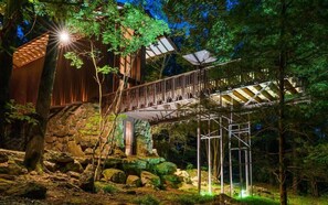 A rustic wooden building with a stone foundation, a wooden deck, and a metal staircase leading to a covered area.