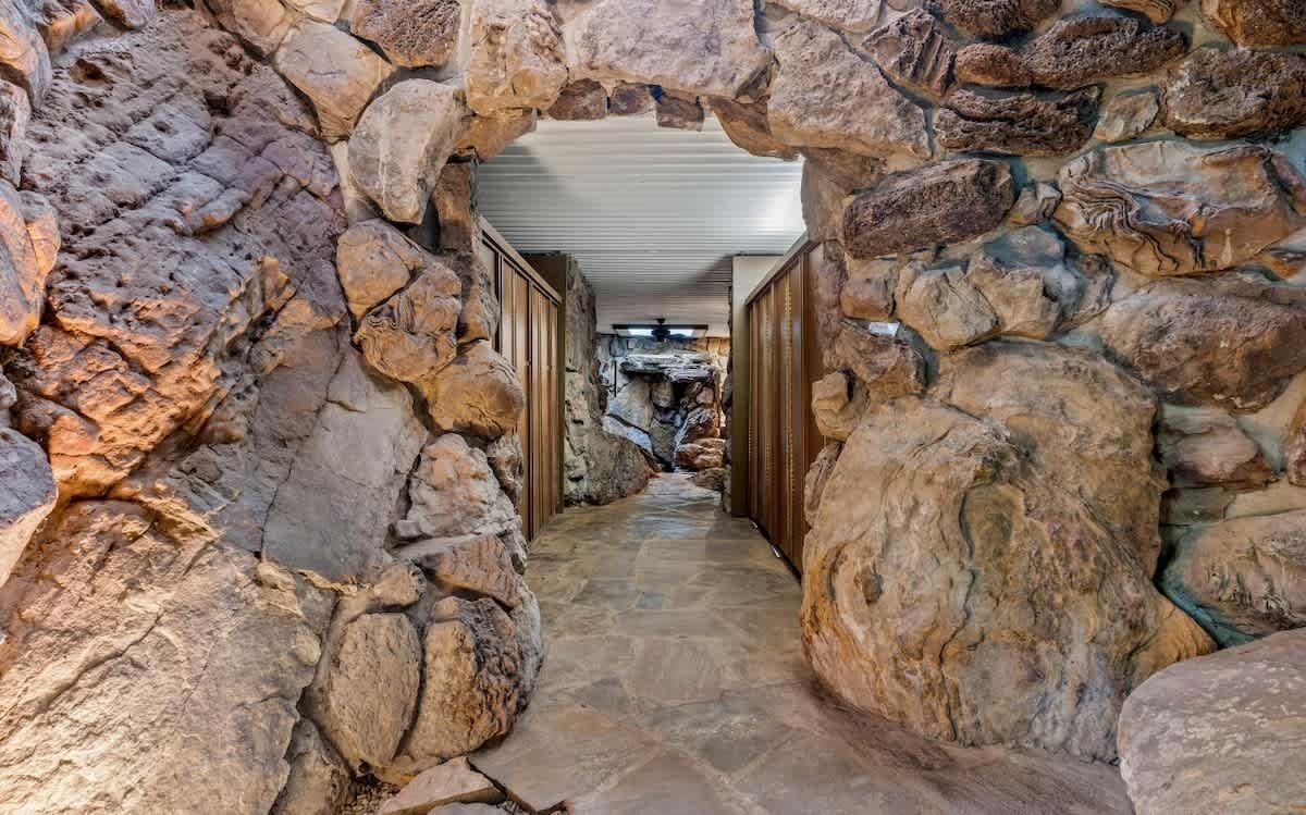 Un pasillo de paredes de piedra con ventilador de techo que conduce a una habitación con chimenea de piedra.