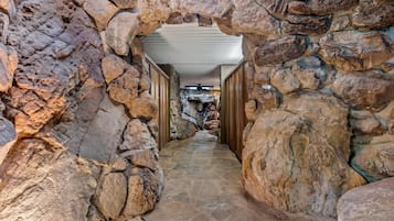 Un pasillo de paredes de piedra con ventilador de techo que conduce a una habitación con chimenea de piedra.