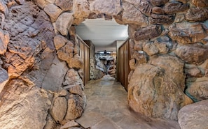 A stone-walled corridor with a ceiling fan, leading to a room with a stone fireplace.