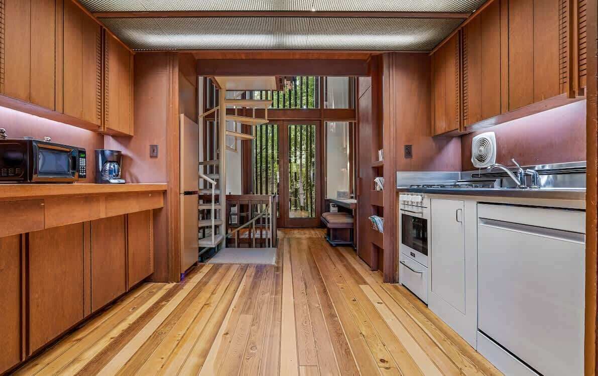 A modern kitchen with wooden cabinetry, a central staircase, and a view of the outdoors.