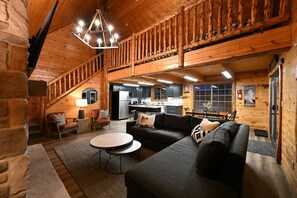 Cozy cabin-style living area with a sofa, coffee table, and staircase leading to an upper level.