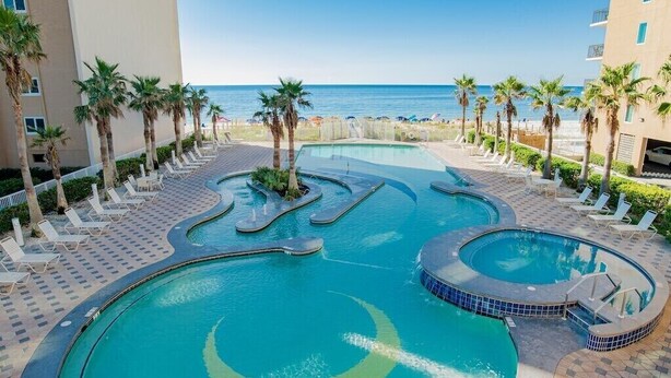 Zona de piscina con varias fuentes y sillones de descanso, rodeada de palmeras y vistas a la playa.