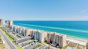 Un hotel costero con varios edificios altos, un estacionamiento y vista a la playa.