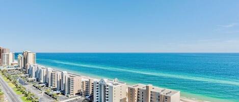 A coastal hotel with multiple high-rise buildings, a parking lot, and a beach view.