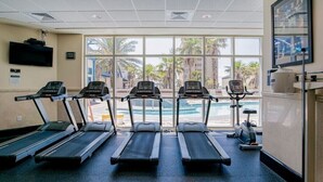 Un gimnasio con cuatro cintas de correr, una bicicleta estática y una piscina visible a través de las ventanas.