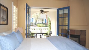 A bedroom with a bed, a ceiling fan, a table, and chairs outside the open door.