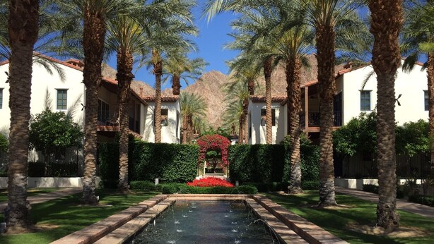 A courtyard with a central water feature, palm trees, and a building with a tiled roof.