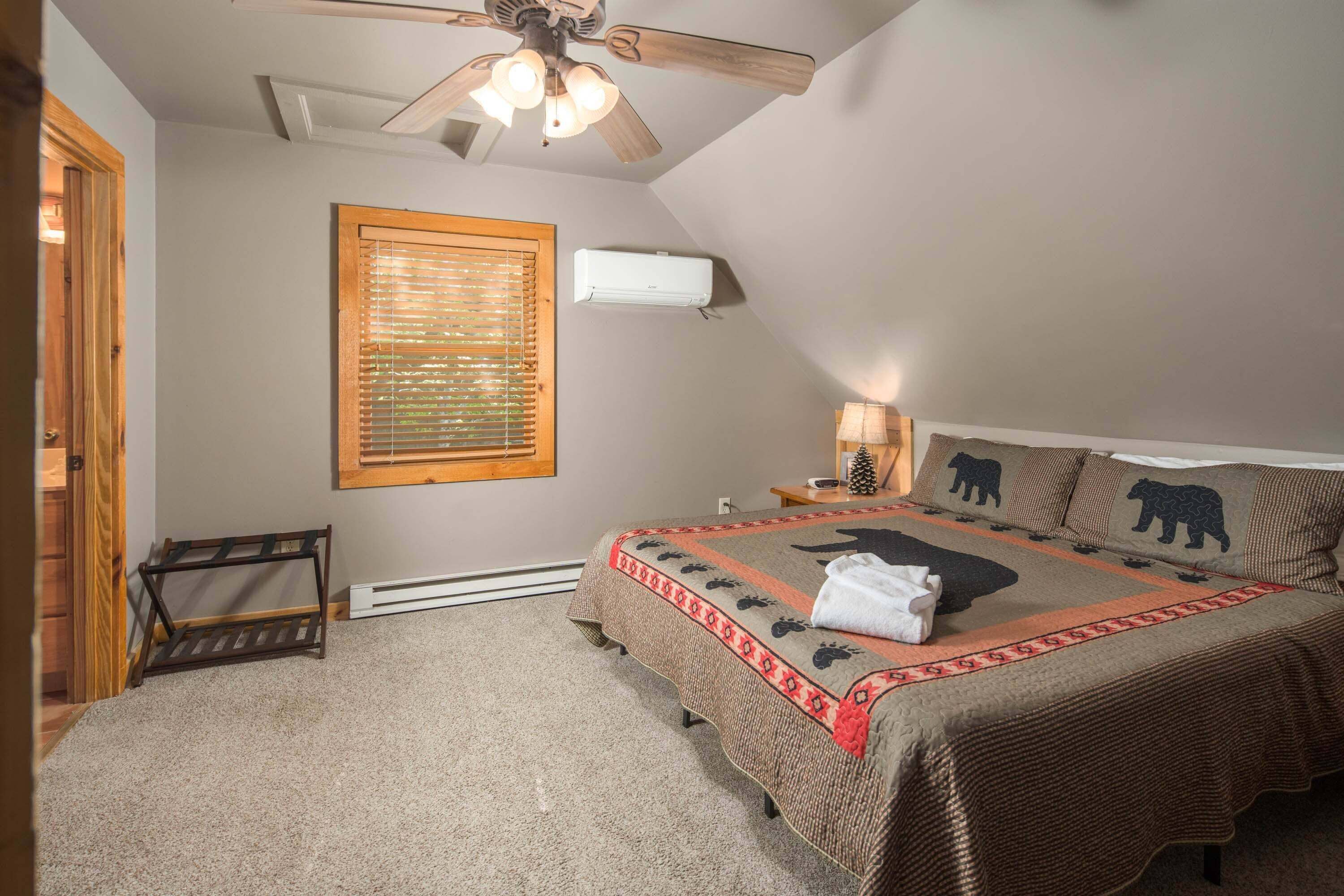 A bedroom with a sloped ceiling, a bed with a bear-themed bedspread, a standing heater, and a ceiling fan.