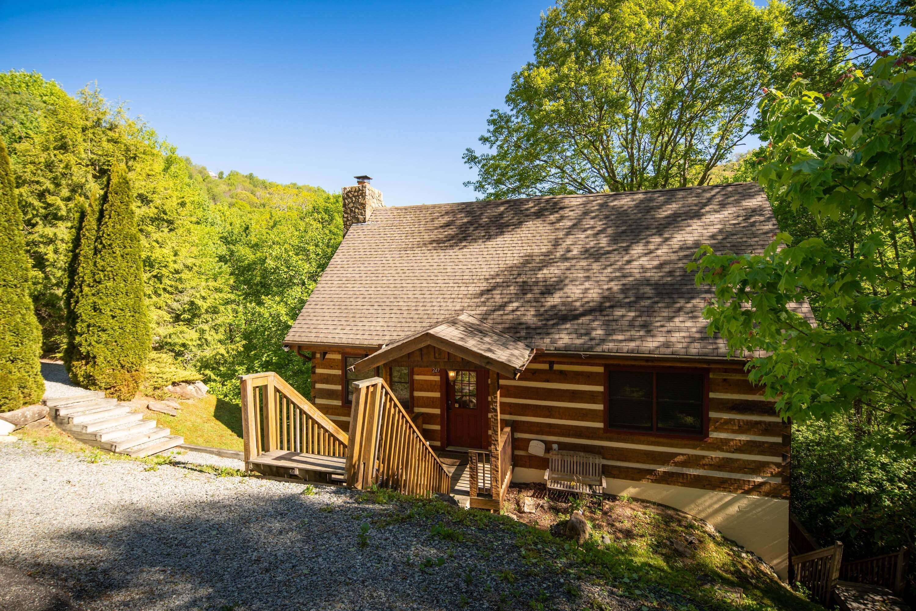 A log cabin with a chimney, wooden porch, and a gravel driveway.