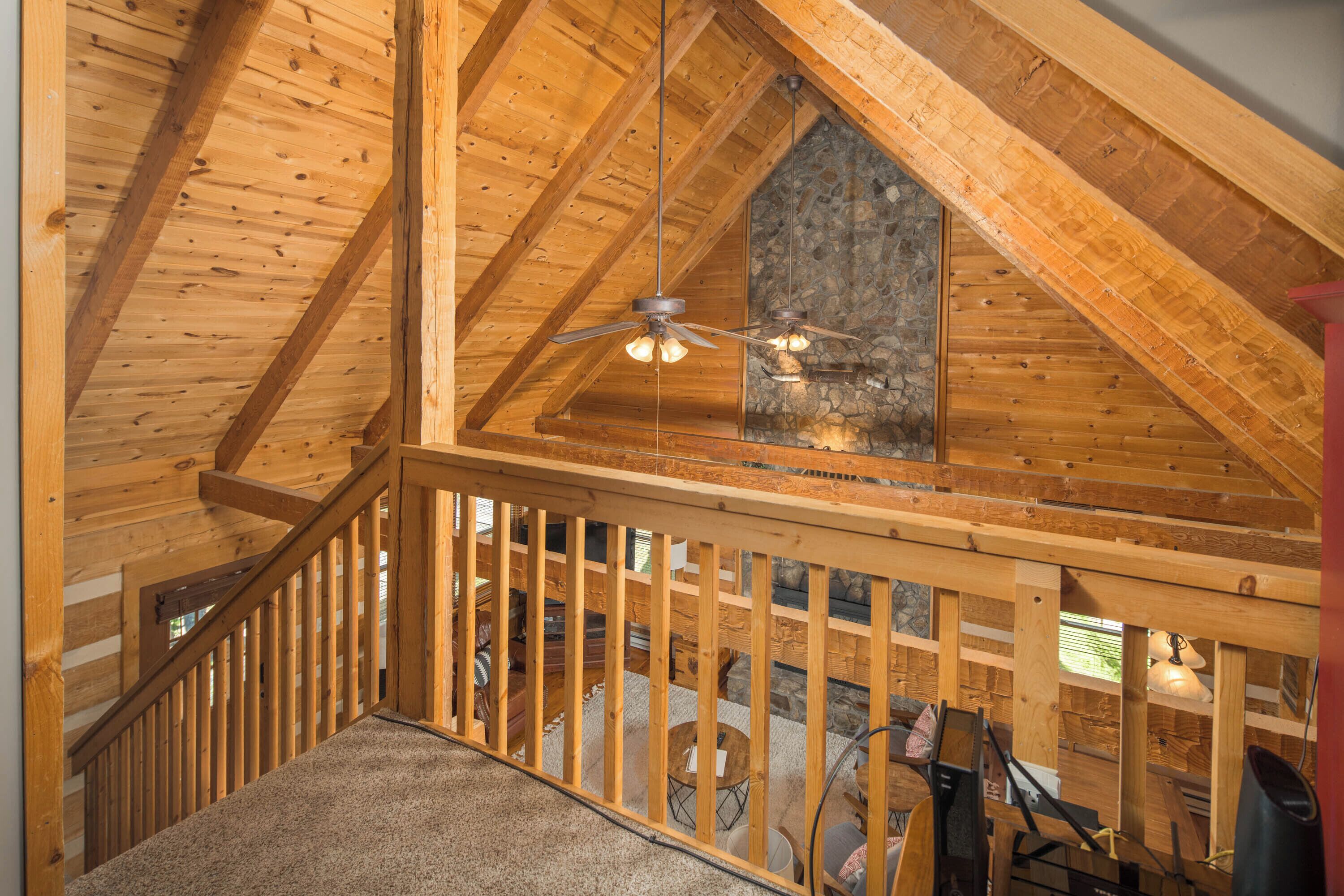 A wooden interior with a sloped ceiling, a stone wall, and a wooden railing.