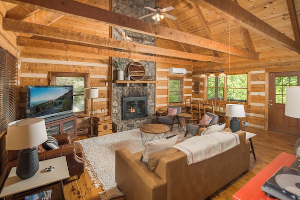 A log cabin interior with a stone fireplace, wooden furniture, a television, and a ceiling fan.