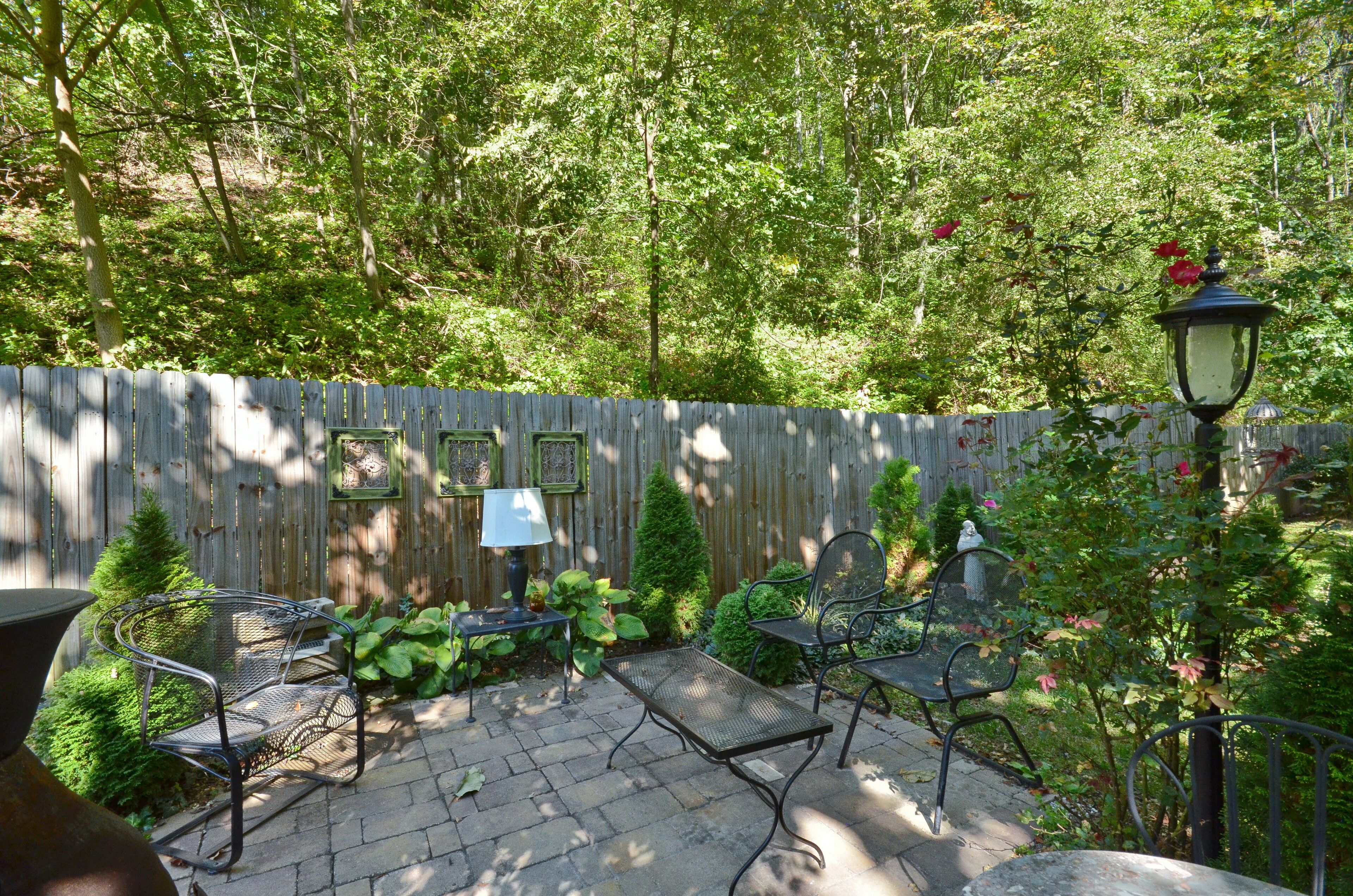 An outdoor patio with metal chairs and a table, surrounded by a wooden fence and greenery.