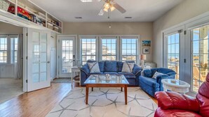A spacious living room with a glass coffee table, blue sofas, and a red chair. - This' L Do - Oceanfront - Upcycled Vintage Beach Cottage (North Topsail Beach)