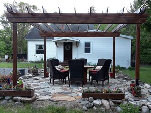 Eine Terrasse im Freien mit Korbmöbeln und Steinboden, umgeben von Blumenkästen und einer Holzw pergola.