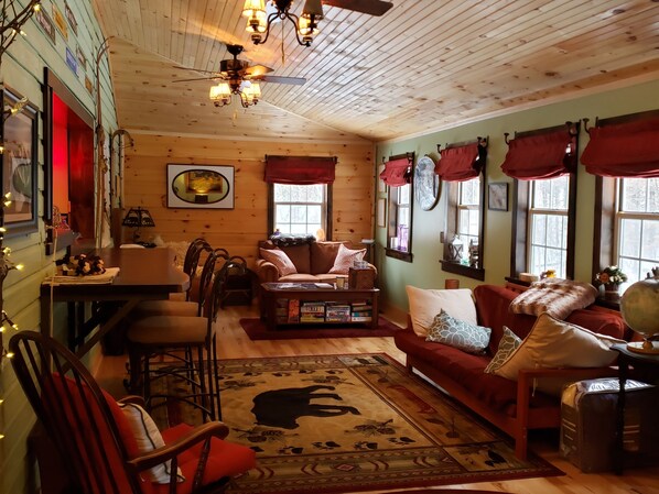 Ein gemütliches Cabin-Interieur mit Holzbalkendecke, Kamin, Sofa, Couchtisch und Teppich mit Bär-Motiv.
