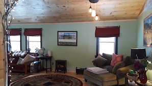 Ein gemütliches Wohnzimmer mit Holzbalkendecke, Kamin, einer Couch, einem Couchtisch und einem Teppich.