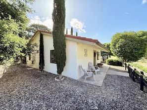 A building with a white exterior, a red roof, and a gravel driveway. There are two white chairs outside.