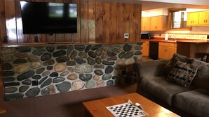 A living room with a stone wall, wooden paneling, a flat-screen TV, a wooden coffee table, and a couch. - Beautiful Vacation Home located on Upper Buckatabon Lake (Conover)