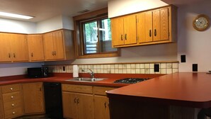 A kitchen with wooden cabinets, a red countertop, a sink, a stove, and a window. - Beautiful Vacation Home located on Upper Buckatabon Lake (Conover)