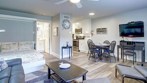 A modern living room with a sofa, coffee table, and TV. There's a dining area with chairs and a kitchen in the background. - Come enjoy one of Port Aransas best hidden gems! Cozy condo, just a block from t (Port Aransas)