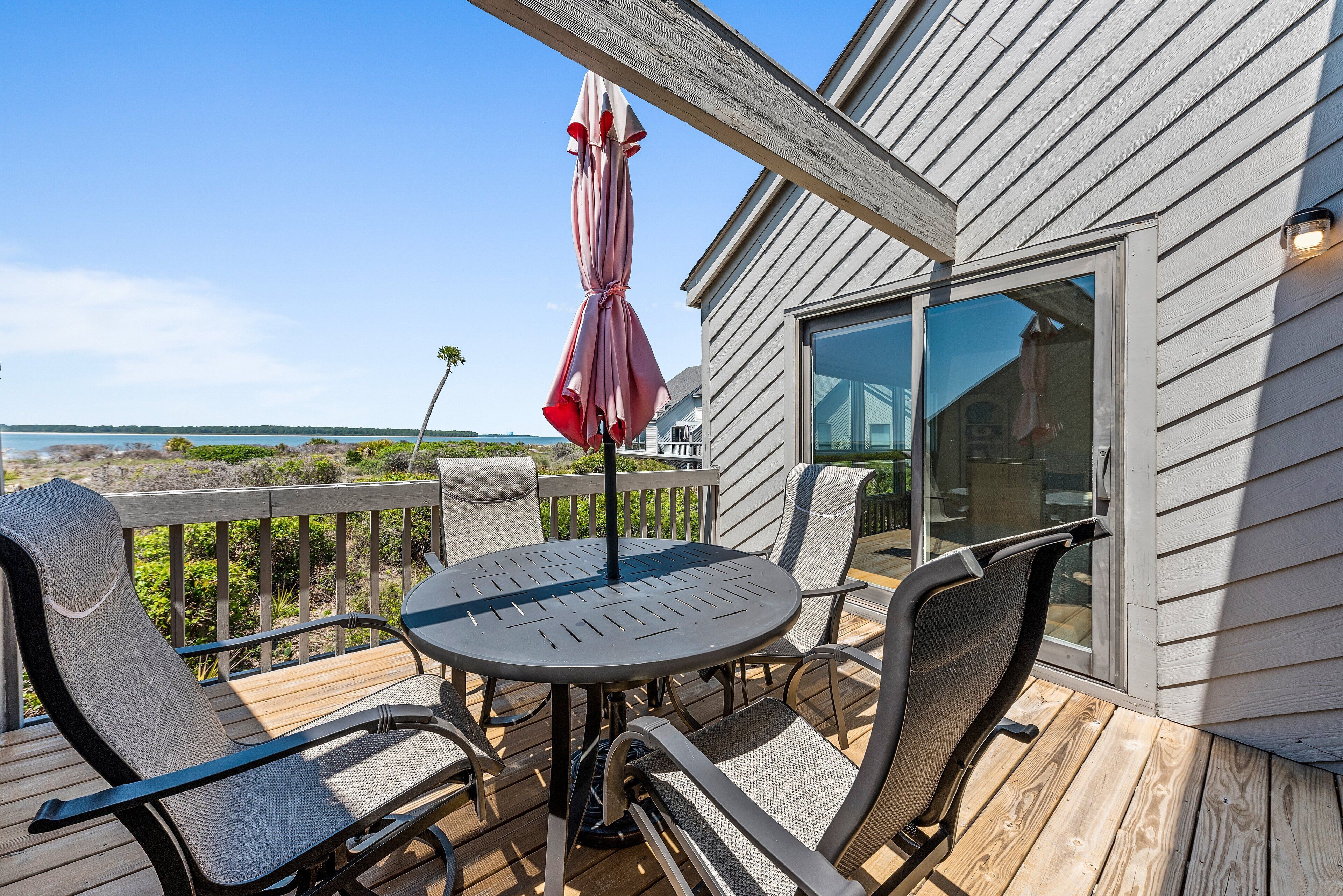 A deck with a round table and chairs, a patio umbrella, and a view of the ocean.