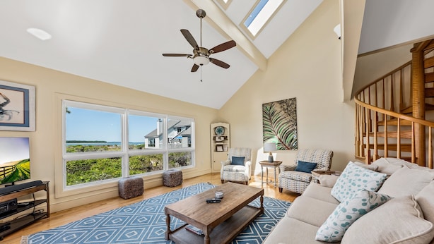 A spacious living room with a large window, a ceiling fan, a wooden coffee table, and a beige sofa. - Waterfront Beach Club Villa! 3 BR/3.5 BA! Luxury, Ocean view! Amenity access included! (Seabrook Island)