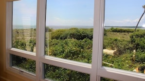A room with three windows overlooking a coastal landscape with dense greenery and a clear view of the sea. - Waterfront Beach Club Villa! 3 BR/3.5 BA! Luxury, Ocean view! Amenity access included! (Seabrook Island)