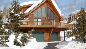 Una baita di legno con un balcone, ampie finestre e un tetto coperto di neve.