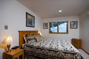 A bedroom with a large bed, a nightstand, a lamp, and a window with a snowy view. - Tree Haus Chalet (Steamboat Springs)
